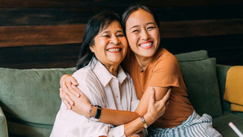 A woman and her mum hug on a couch.