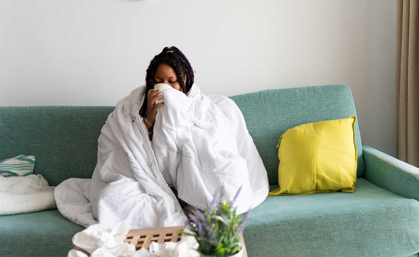Woman sniffling while sitting on a couch with a blanket around her body