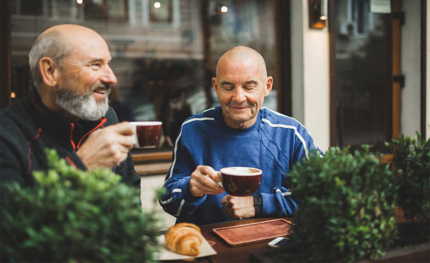 Two elderly men sitting with coffee cups in hand