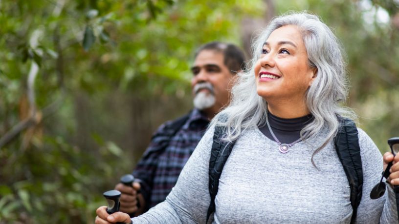 A man and woman smile as they hike through the bush.