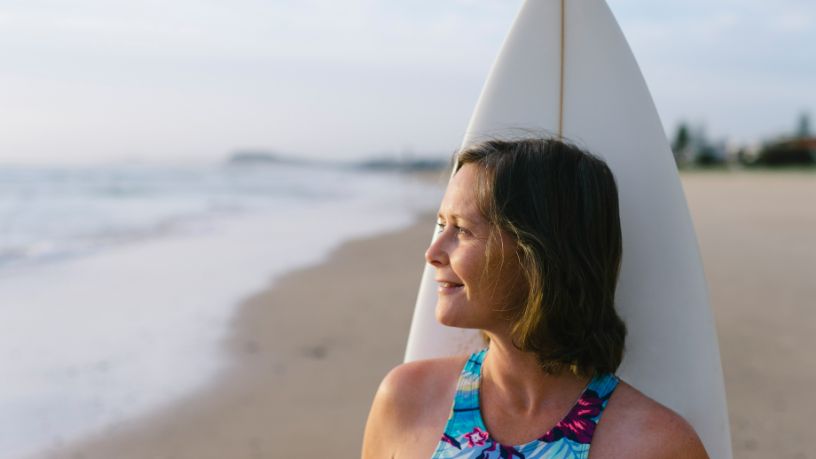 A woman stands in front of a surfboard on a beach.