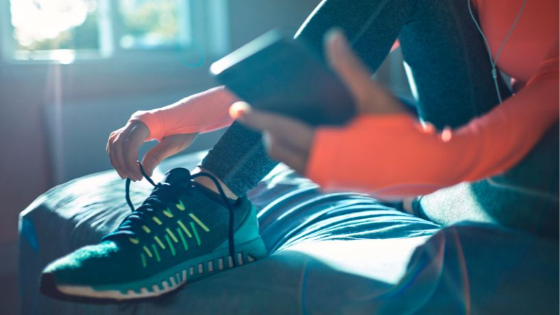 A person with headphones on tying their shoelaces before exercising