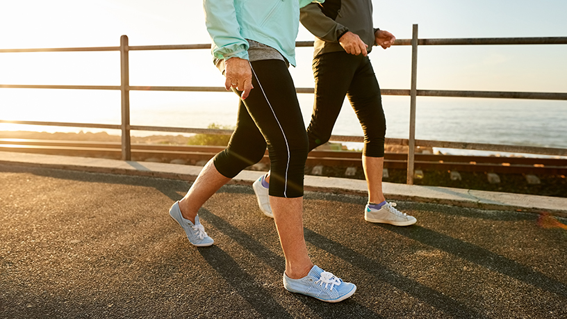 Two women walking by the ocean with a focus on their legs. 