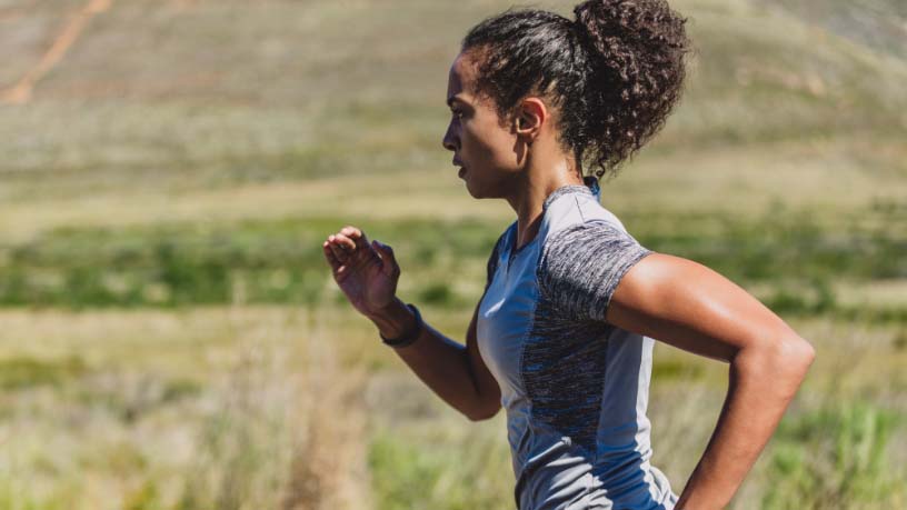 A woman jogs next to an open field.