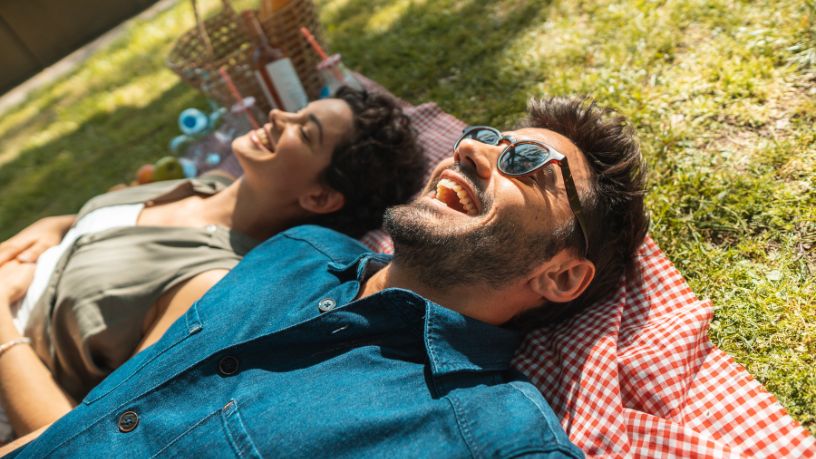 A man and a woman laying on a picnic rug together.