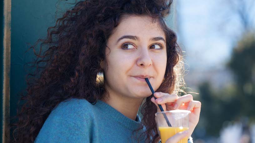 A woman drinks an orange-based mocktail and glances to the side. 