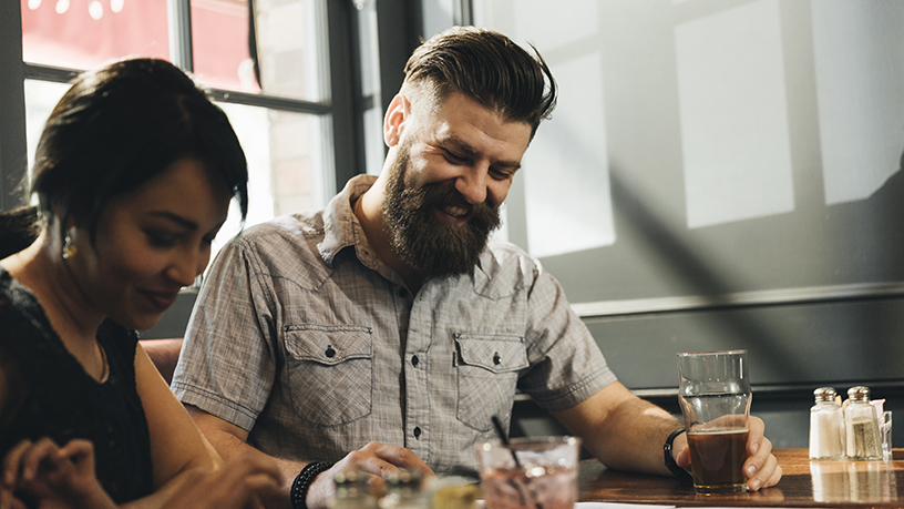 Man and woman sitting at a table with drinks and laughing