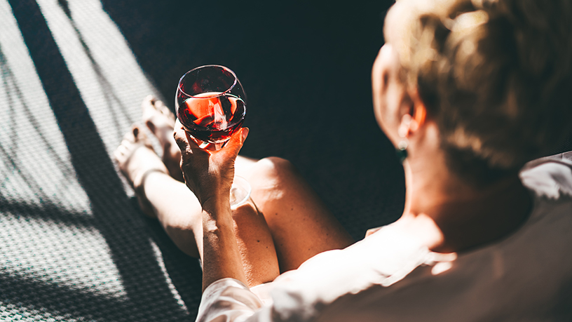 A women sitting down and looking away with a glass of red wine in her hand.