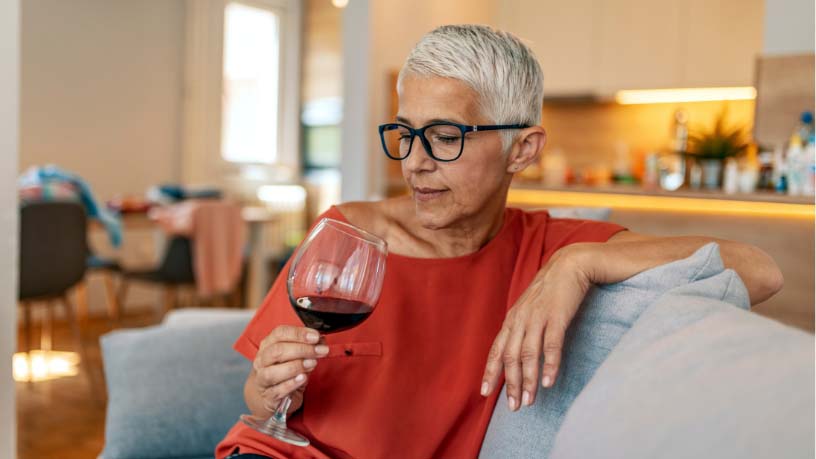 A woman sits on a couch looking at a glass of wine.