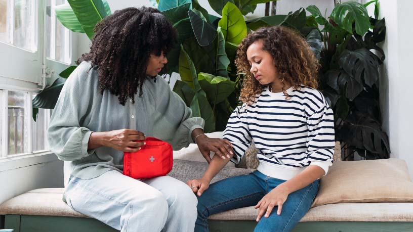 A woman holds a first aid kit and checks her daughter’s arm.