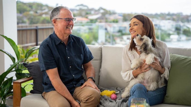 Smiling woman holding a dog while seated on a couch with a man.