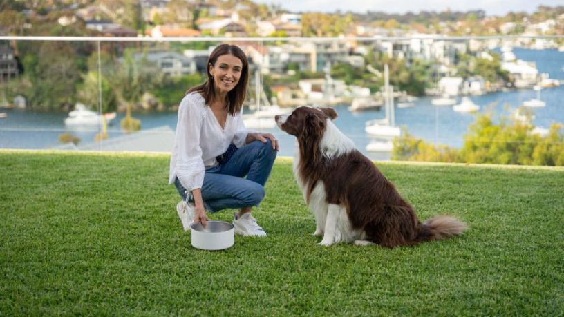 Woman holding a dog bowl with dog by her side.