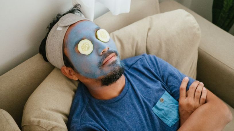 Man with facemask and cucumber on his eyes.
