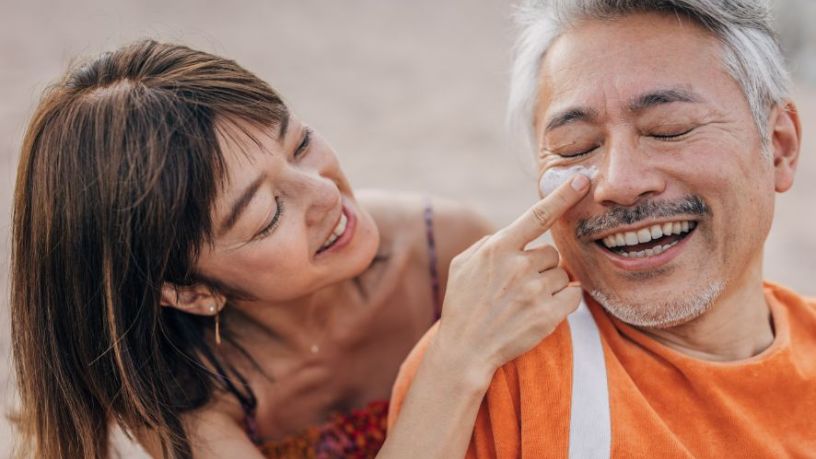 Woman applies sunscreen to man’s face.