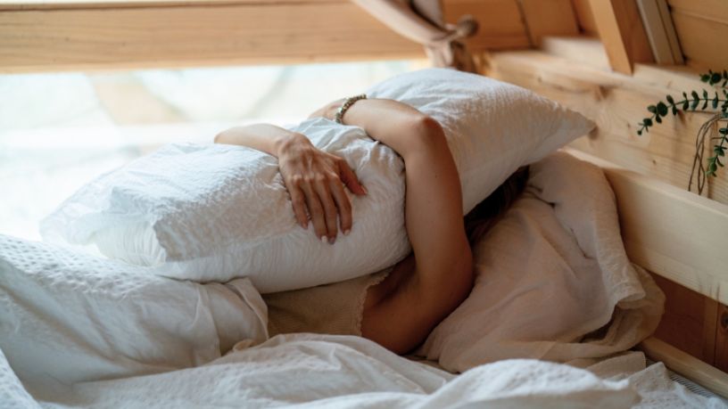 Woman in bed with pillow over her face.