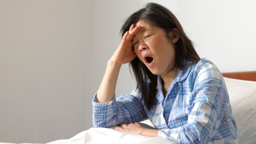 A woman sits up in her bed and yawns.