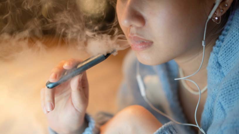 A girl vapes with her headphones on.