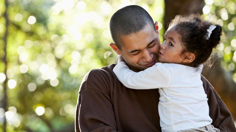 A man hugs his daughter and ducks his head.
