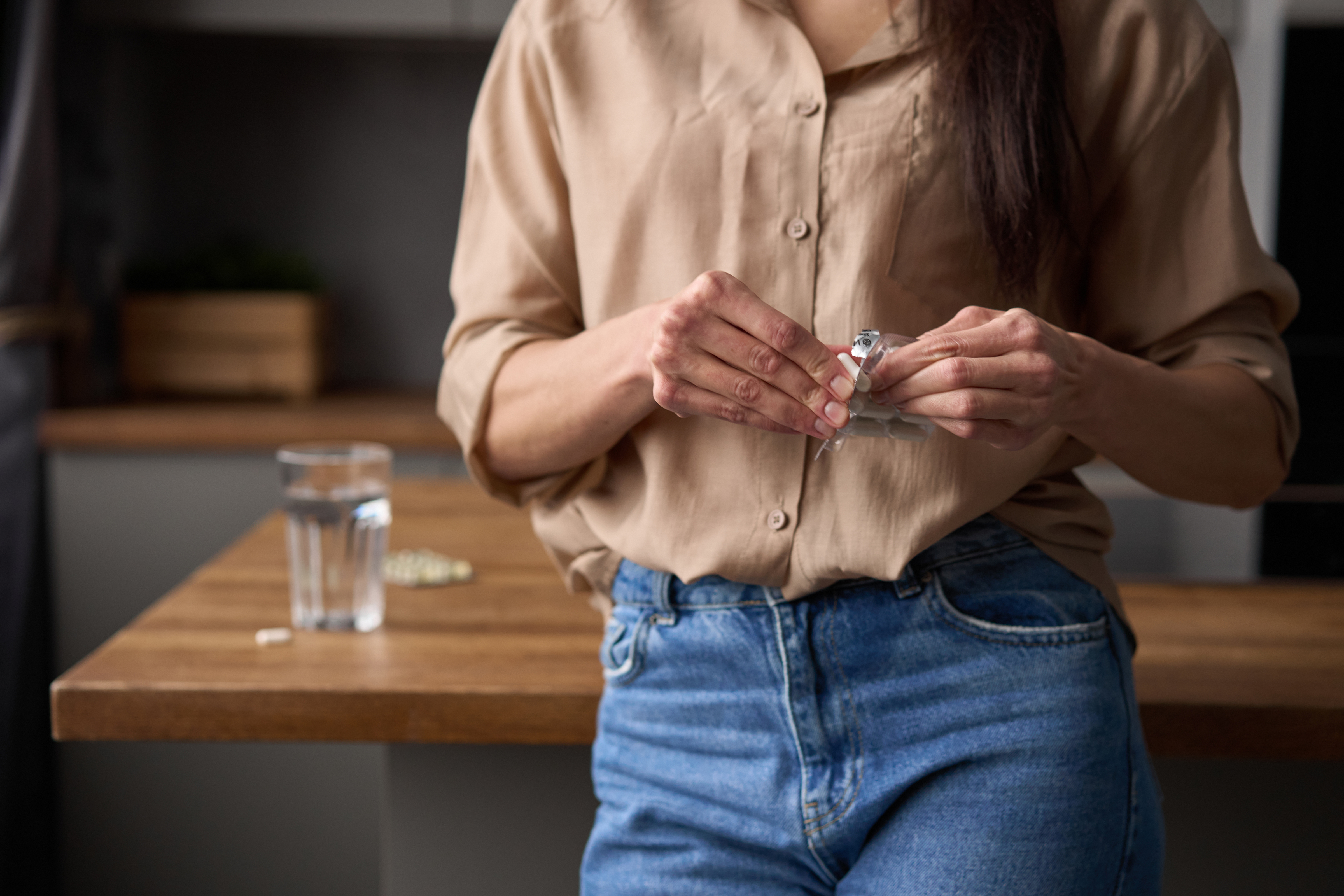 A lady standing by the kitchen bench with medication on her hands. 