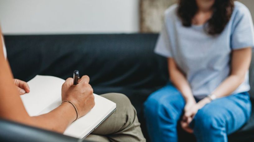 A person takes notes with a pen as they speak with a patient.