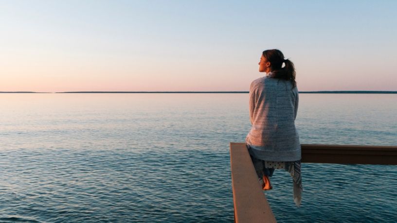 A woman sits on a wooden fence overlooking the ocean.