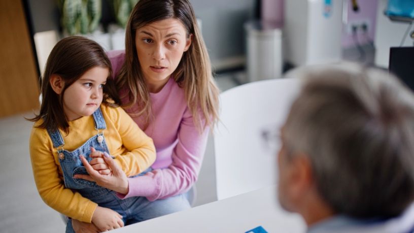 A woman holds her toddler as she speaks to a doctor.