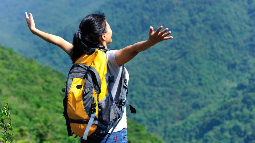 A hiker stands at the top of a mountain with her arms outstretched in joy.