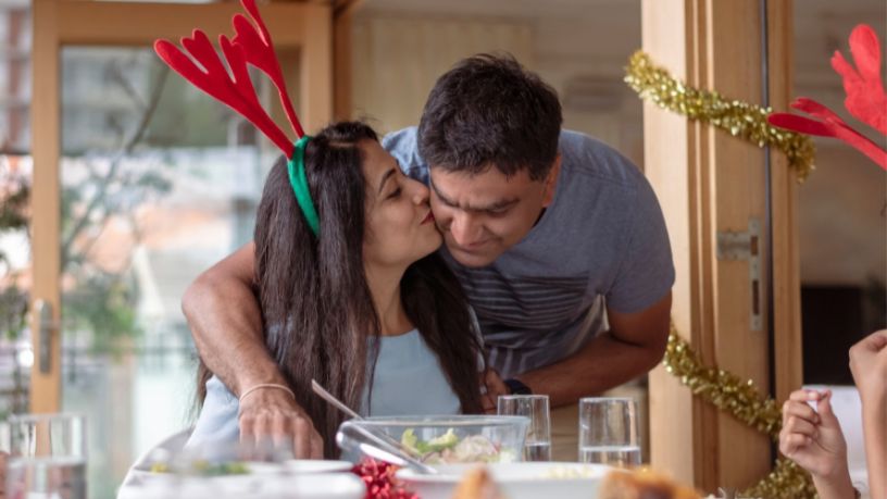 A woman kisses her partner’s cheek as he leans down.