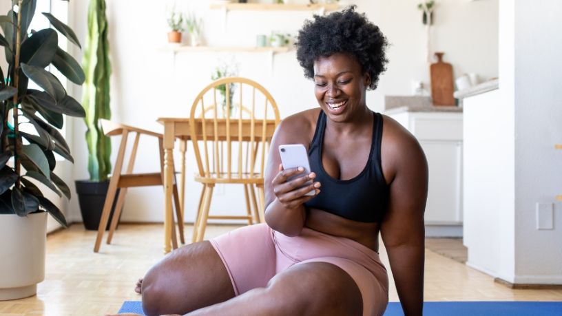 A woman in workout gear smiles at her phone.