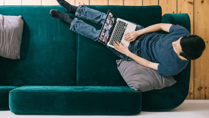 A man uses his laptop with his feet propped up on his couch.