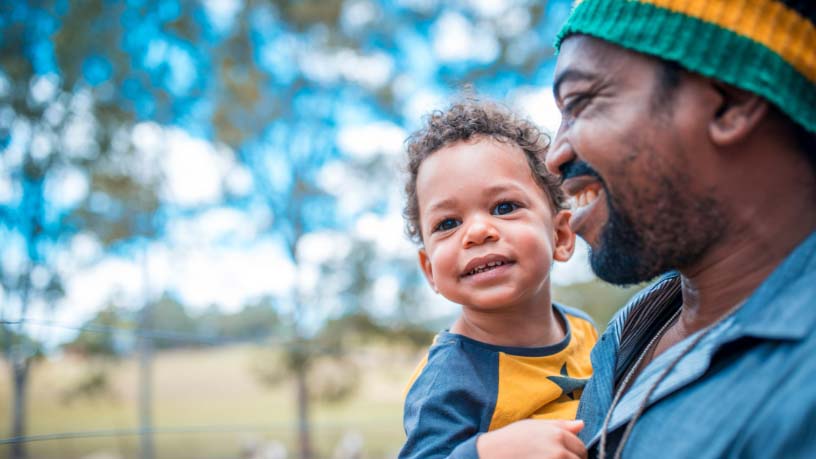 A man holds his baby in the woods and laughs.