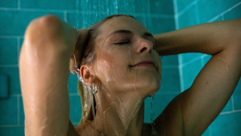 A woman holds her head as she stands in the shower.