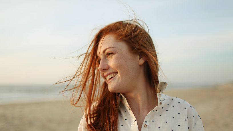 A woman stands on a beach and smiles.