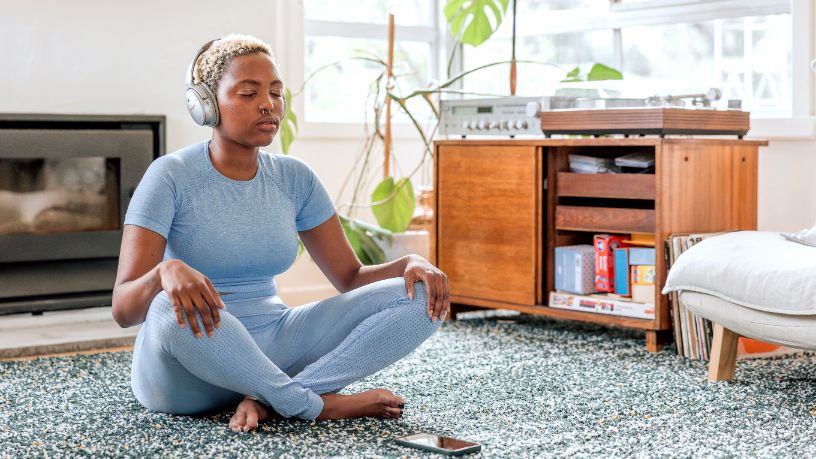 A woman wearing headphones meditates in her lounge room.
