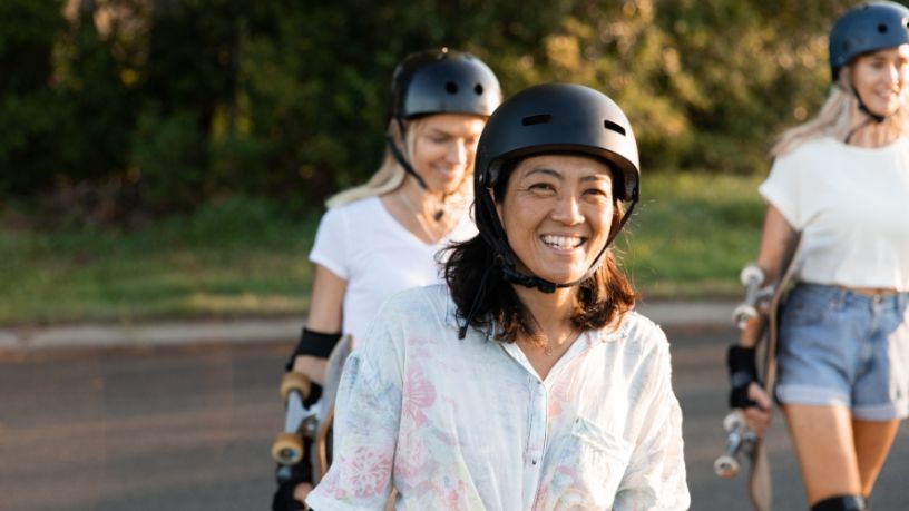 Three skateboarders walk through a park on a sunny day.