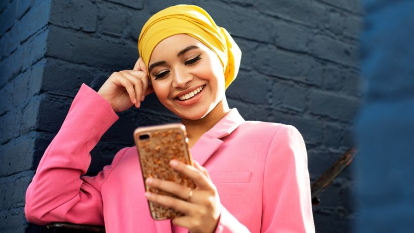 A woman wearing a headscarf looks at her phone and smiles