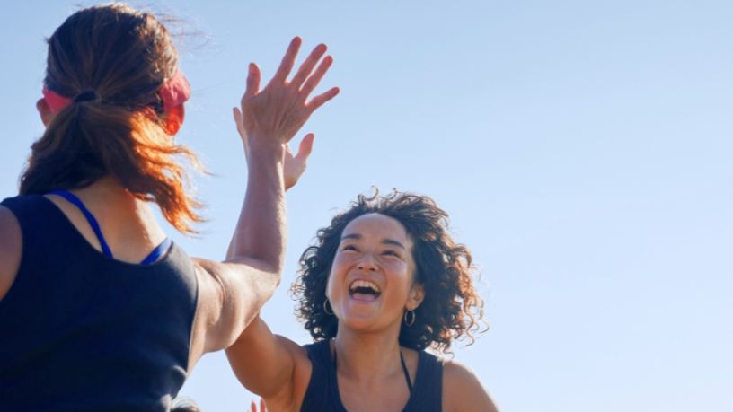Two women in activewear give each other a high five.