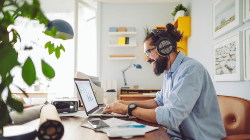 A man sits at a home office working on a laptop.