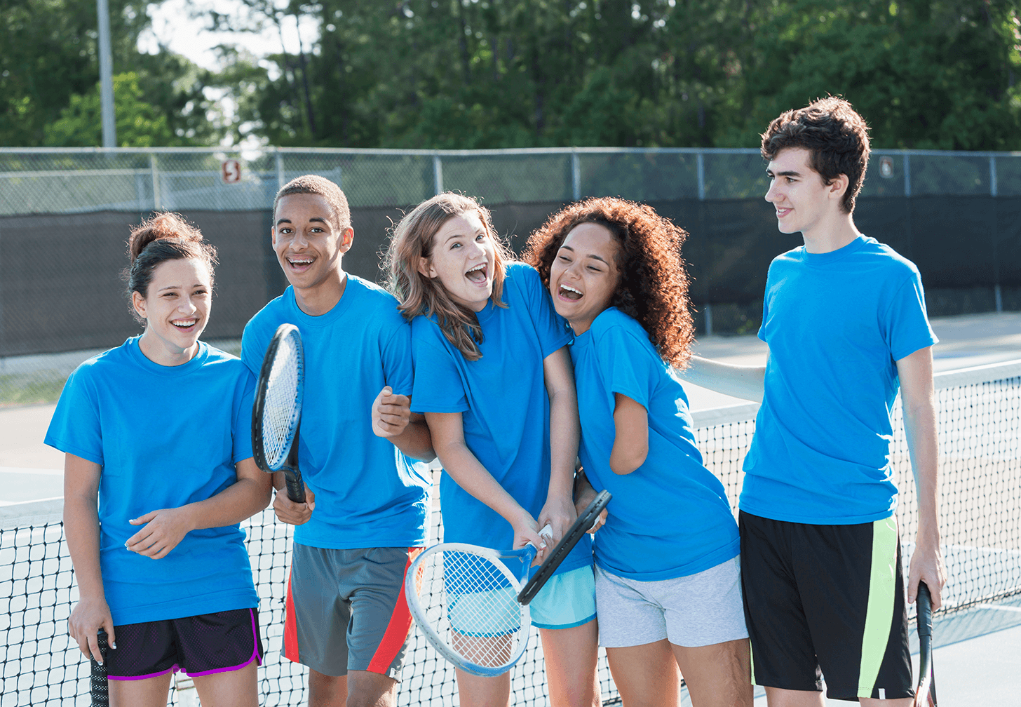 Children wearing blue sports uniforms smiling and standing together on an outdoor court, promoting inclusive sport for all abilities.