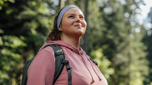 A woman wearing a backpack exercising outdoors in a park setting.