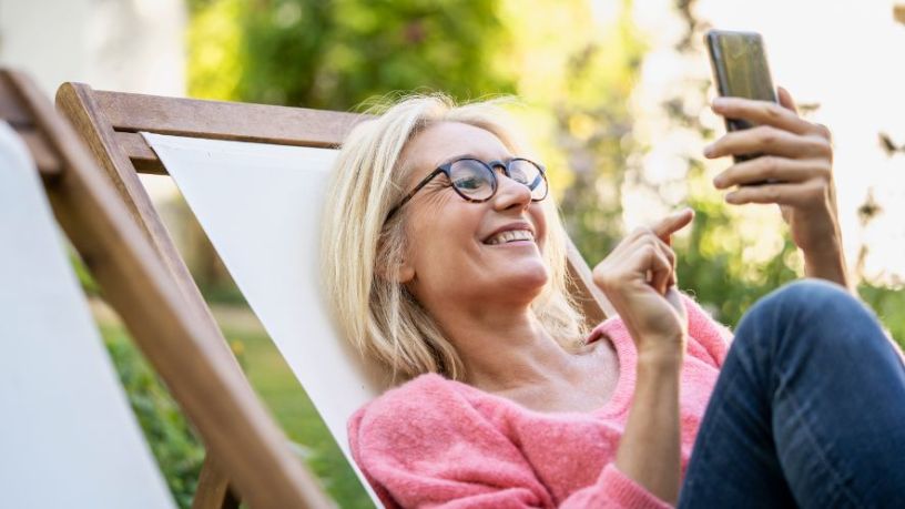 A woman reclines in a chair and smiles as she looks at her phone.