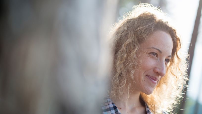 A woman with sun in her hair smiles.