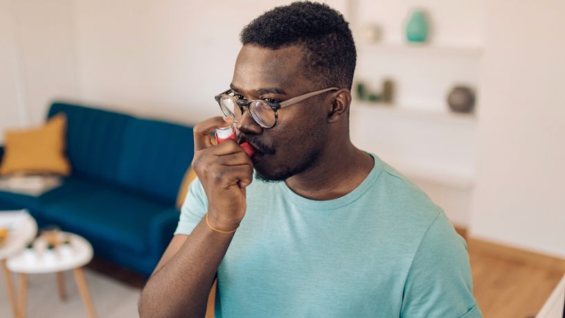 A man stands in his living room and uses an inhaler.