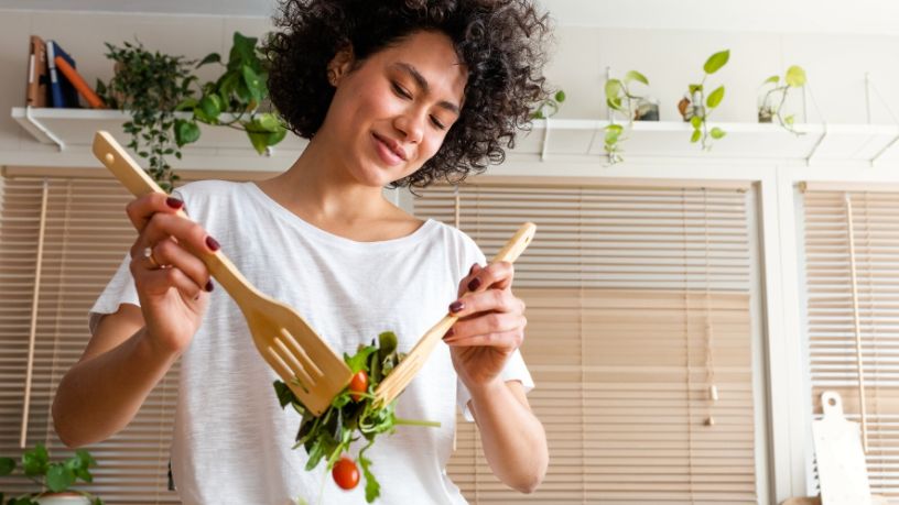 A woman tosses a salad with 2 salad forks.