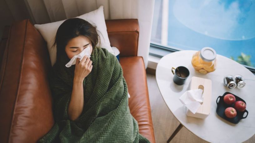 Woman lays on couch blowing her nose.