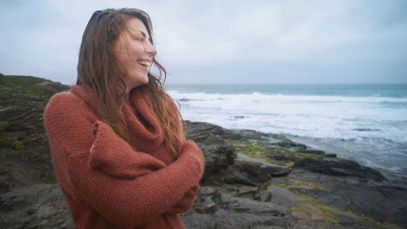 A woman stands by the ocean as clouds roll in.