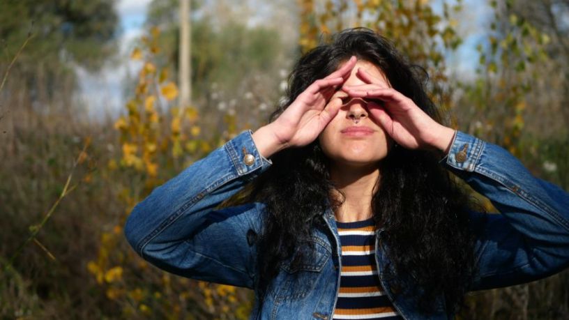 A woman standing outside rubs at her eyes.