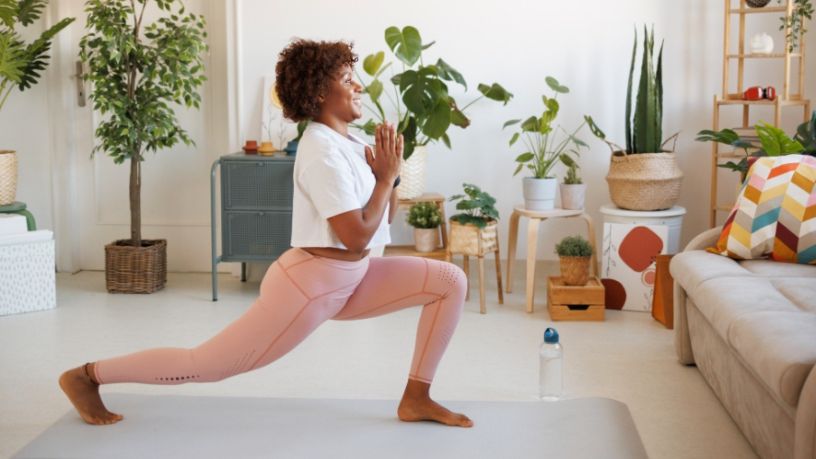A woman holds a pose on a yoga mat inside her living room.