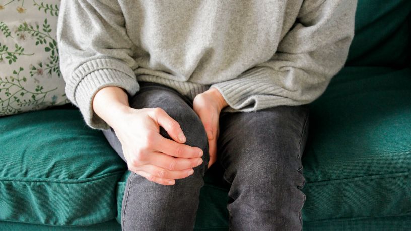 A person sitting on a green sofa holds their knee.