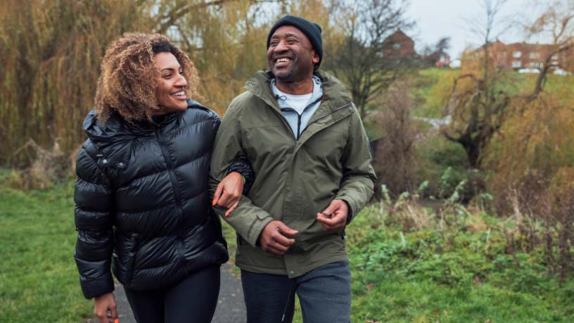 A couple linking arms walks along a path.